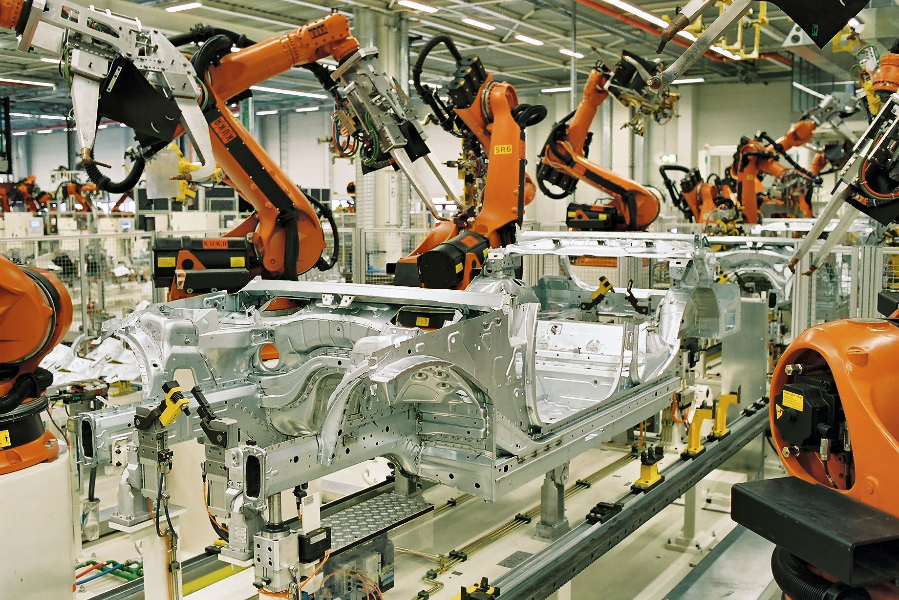 Industrial robots spot-welding car bodies on an automotive assembly line — lights-out manufacturing at fleet scale
